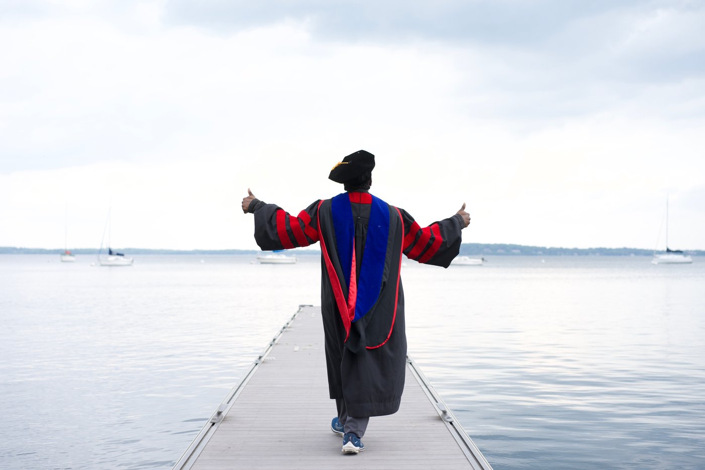 Maxwell O. Chibuogwu in doctoral regalia in front of UW-Madison 2024 sculpture